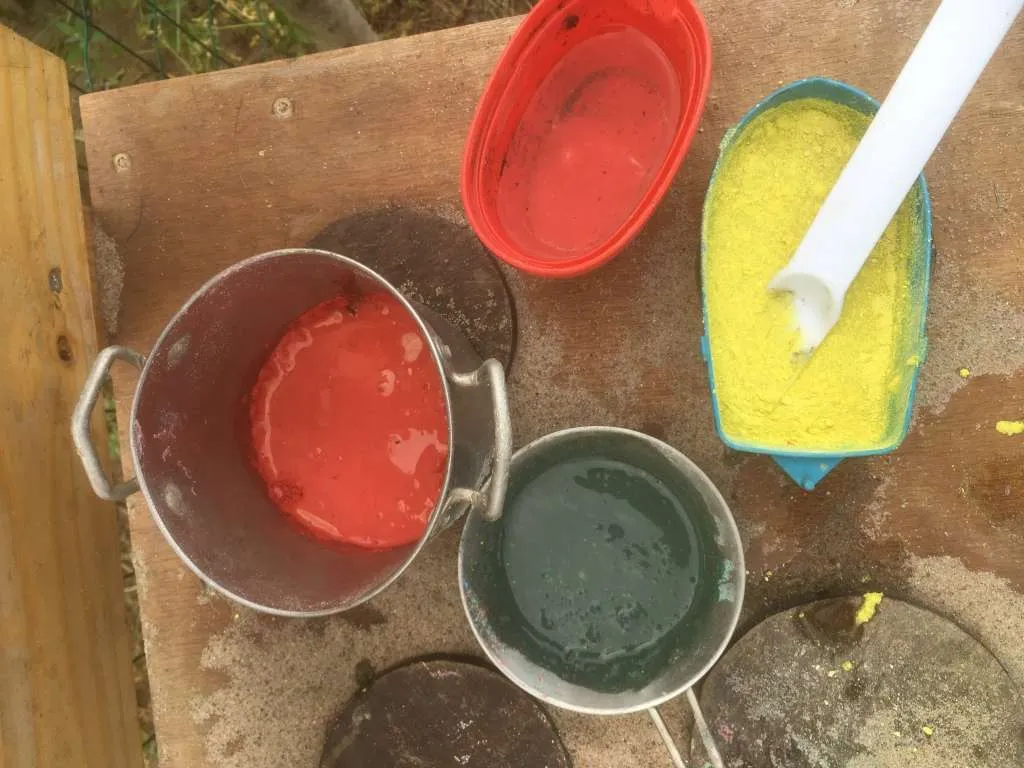  verf maken: Water bij het krijtpoeder mengen in de pannetjes van de modder keuken. Zo wordt het stoepkrijt, stoepverf!